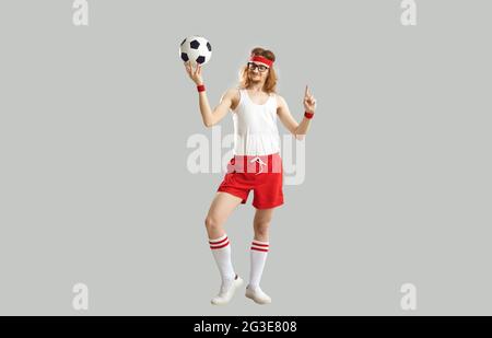 Drôle nerdy jeune homme en lunettes, débardeur, short et serre-tête tenant le ballon de football Banque D'Images
