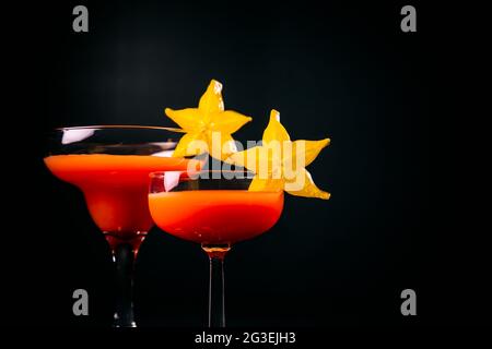 Cocktail rouge décoré d'étoiles de fruits sur fond noir. Banque D'Images