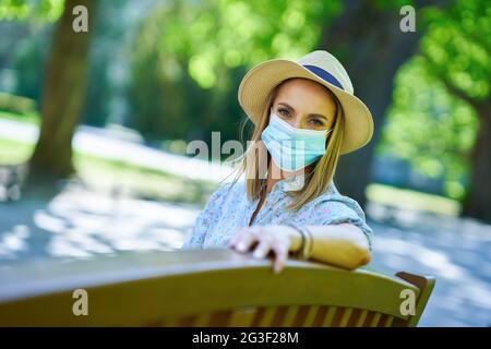 Femme en masque assise sur un banc dans le parc. Banque D'Images