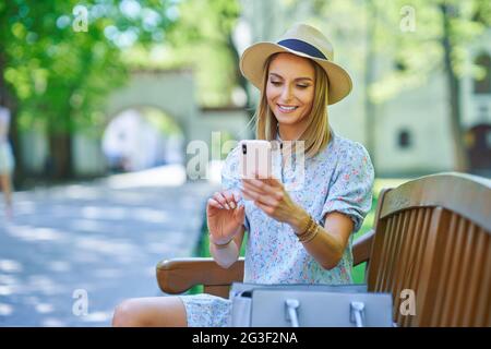 Une fille assise sur un banc avec un smartphone Banque D'Images