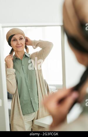 Portrait vertical d'une femme mûre mettant sur le foulard tout en regardant le miroir et en se préparer à sortir Banque D'Images