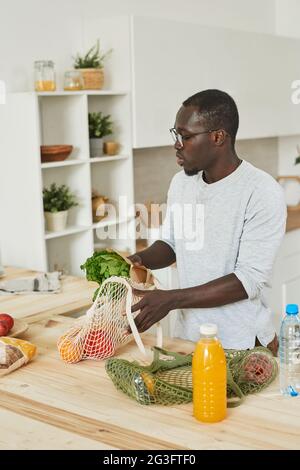 Un jeune Africain assis à la table et préparant la nourriture pour le dîner dans la cuisine Banque D'Images