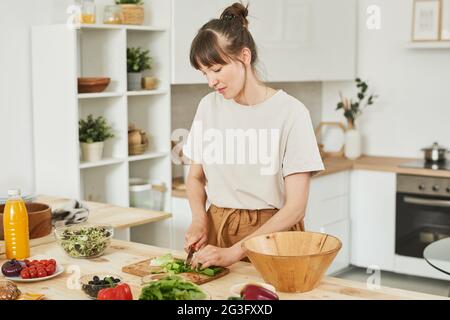 Une jeune femme coupe la salade à bord et prépare la salade de légumes pour le dîner Banque D'Images