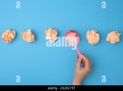 la main femelle tient une loupe sur des boules de papier froissés. Concept de recherche et de sélection d'idées, brainstorming, résolution de problèmes en busine Banque D'Images