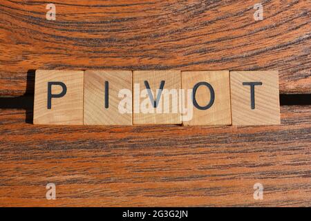 Pivot, mot à la mode d'affaires en lettres d'alphabet de bois isolées sur fond de bois de teck Banque D'Images