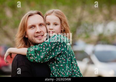 Jolie fille qui épouse doucement son père élancé en ville et regarde l'appareil photo sur un arrière-plan flou Banque D'Images