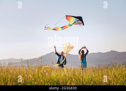 Fille avec un père souriant pendant qu'ils volent un cerf-volant coloré sur la prairie haute herbe dans les champs de montagne. Des moments chaleureux en famille ou en plein air s Banque D'Images