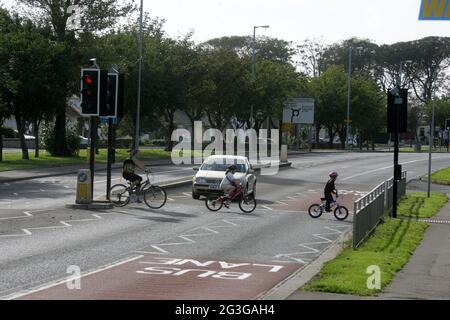 A78 Stevenston, North Ayrshire, Écosse. Royaume-Uni enfants à vélo traversant la route du tronc en utilisant le Pelican Crossing. Un passage à niveau en pélican est le nom britannique et irlandais d'un type de passage à niveau pour piétons, qui comprend une paire de pôles chacun avec un ensemble standard de feux de signalisation faisant face à la circulation venant en sens inverse, un bouton-poussoir et deux pictogrammes lumineux de couleur faisant face au piéton de l'autre côté de la route. Banque D'Images