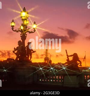 Gros plan sur une colonne de lampadaire ornée de statues et d'étoiles sur un groupe de rues illuminées le soir Lumières avec la Tour Eiffel sur l'horizon paysage urbain au coucher du soleil crépuscule ciel partie de l'historique Alexandre III pont de route au-dessus Rivière Seine visible à travers le pavé de pierre balustrade ville de Paris France Banque D'Images