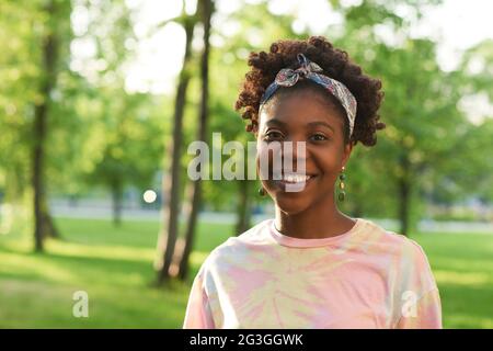 Portrait d'une jeune femme africaine souriant à la caméra tout en marchant dans le parc Banque D'Images