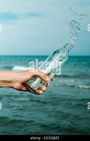 gros plan d'un homme qui verse de l'eau dans une bouteille d'eau réutilisable en verre en face de l'océan Banque D'Images