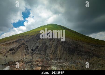 Vue sur l'un des sommets du volcan Lokon, et le paysage accidenté de ses pentes verdoyantes, couvertes de nuages sombres, Indonésie Banque D'Images