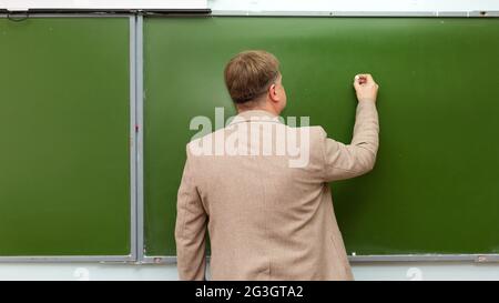 Un professeur de mathématiques écrit de la craie sur l'espace de copie du tableau noir. Banque D'Images