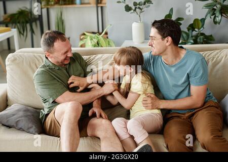 Bonne famille gay jouant avec la fille adoptée sur le canapé à la maison Banque D'Images