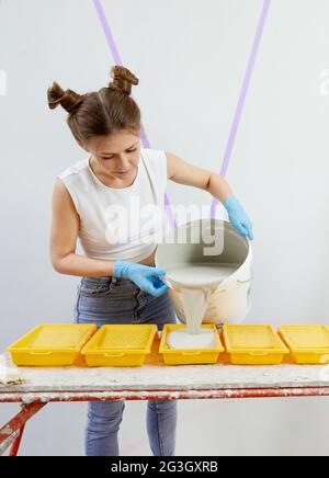Une jeune femme verse de la peinture dans un bac à peinture en plastique Banque D'Images