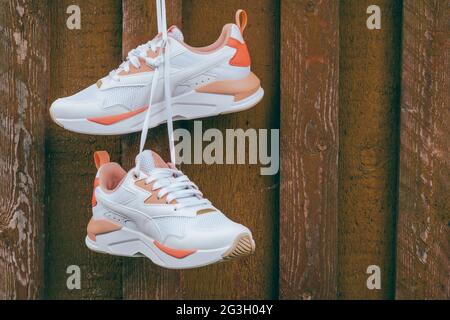 Sneakers blanches pour femme avec inserts de corail accrochés à l'ongle sur un mur de planches en bois rustique brun Banque D'Images