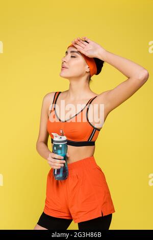 femme fatiguée avec bouteille de sport tenant la main près du visage isolé sur jaune Banque D'Images