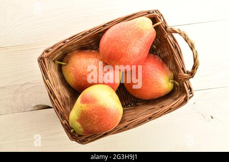 Plusieurs poires mûres jaune-rouge dans un panier, sur une table en bois, vue de dessus. Banque D'Images