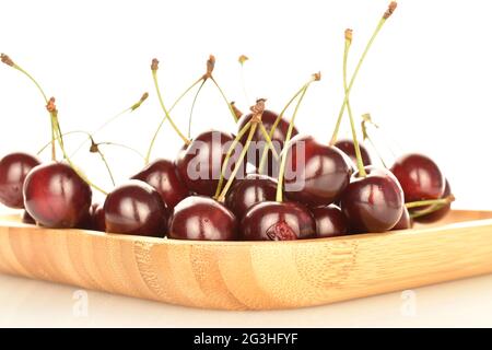 Plusieurs cerises mûres baies sur une plaque de bambou, gros plan, sur fond blanc. Banque D'Images