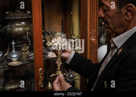 16 juin 2021, Irak, Mossoul : le Fakhri Suleiman Al-Tai irakien tient une sculpture métallique représentant la Crucifixion de Jésus près d'un cabinet rempli d'autres pièces anciennes qu'il a recueillies après son retour dans la vieille ville de Mossoul après sa libération de la soi-disant organisation terroriste de l'État islamique (EI). Al-Tai a décidé de convertir sa maison en musée temporaire où il expose plus de 5,000 pièces reflétant l'héritage et l'histoire de Mossoul, qui a été gravement endommagé entre 2014 et 2017 sous le règne de l'État islamique. Al-Tai a dépensé près de 33,000 dollars US à la poursuite de sa passion Banque D'Images