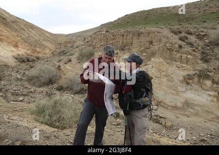 Randonneurs, hommes, adultes âgés de 60 et 70 ans regardent une carte tout en se reposant sur une randonnée dans un lit de rivière sec près de Wadi qelt, désert de Judée, Cisjordanie. Banque D'Images