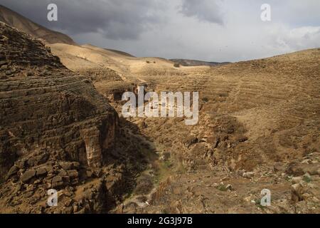 Vue panoramique sur le ravin de Wadi Qelt dans le désert de Judée et son terrain extrême et accidenté admirez les nuages d'hiver et les zones de lumière et d'ombre Banque D'Images