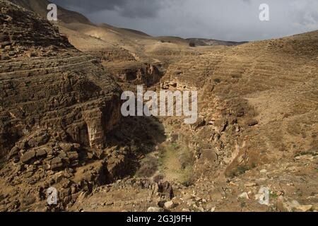 Vue panoramique sur le ravin de Wadi Qelt dans le désert de Judée et son terrain extrême et accidenté admirez les nuages d'hiver et les zones de lumière et d'ombre Banque D'Images