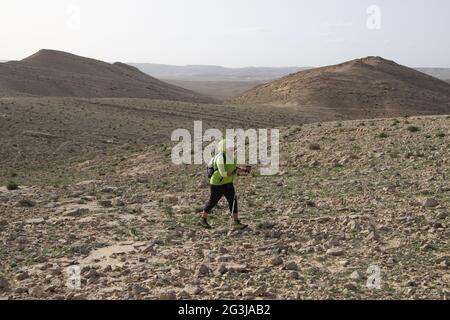 Randonneur en équipement de randonneurs, adulte âgé de 55 ans, marche sur un terrain rocheux en utilisant ses bâtons de randonnée. Près du grand Makhtesh, le désert du Néguev, Israël Banque D'Images