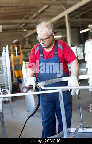 Employé de collier bleu pour polir un morceau de métal dans une usine de fabrication. L'artisan Polisseuse est occupé et concentré dans une usine. Banque D'Images