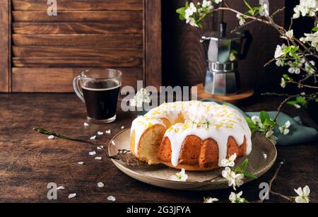 Petit gâteau au citron frais maison décoré de glaçure blanche et de zeste sur un fond rustique en bois avec des branches de prune en fleur. Banque D'Images