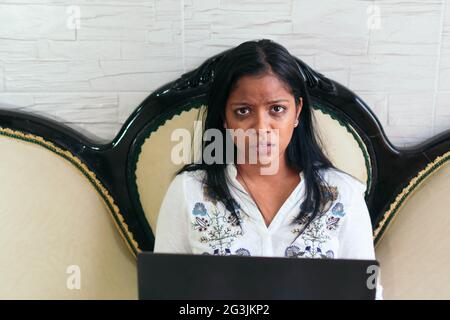 Une fille triste travaille à la maison, s'assoit sur le canapé et regarde dans la caméra. Banque D'Images