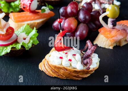 Sandwich espagnol créatif qui ressemble à un bateau avec une voile, composé de fromage à la crème, radis, poivre rouge, et pieuvre avec des tentacules Banque D'Images