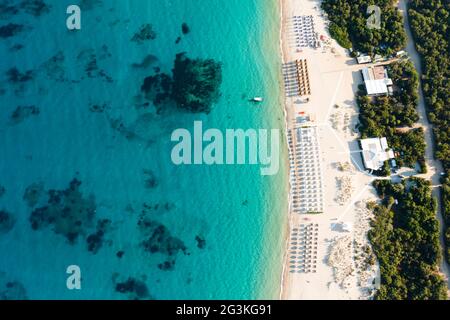 Vue d'en haut, vue aérienne sur une plage de sable blanc vide avec parasols de plage et turquoise, eau claire pendant le coucher du soleil. Banque D'Images