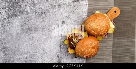 Hamburgers faits maison avec fromage, concombres marinés et oignons roses sur une petite planche à découper en bois sur fond gris foncé. Vue de dessus, plan d'appartement Banque D'Images