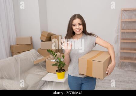 Jolie Jeune femme debout avec boîte en carton à la main montrant ok avec ses doigts. Banque D'Images