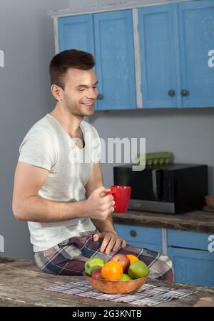 Homme assis sur table en pyjamas, holding red cup. Banque D'Images