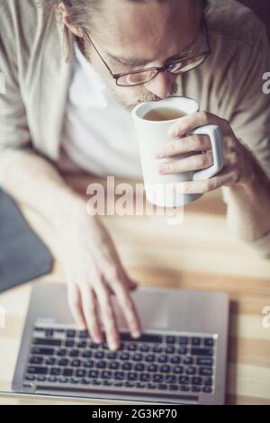 Vue rapprochée de l'homme indépendant dactylographiant sur ordinateur portable, buvant du thé. Banque D'Images