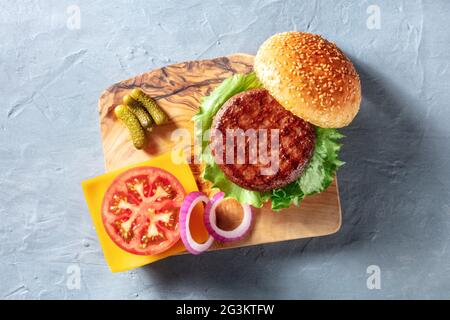 Ingrédients de Burger, tiré par le haut sur un panneau de bois. Patty de bœuf avec salade verte, tomate, oignon, cheddar et petits pains au sésame, grenaille au-dessus Banque D'Images