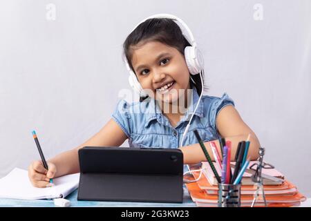 Une jolie petite fille indienne fréquentant un cours en ligne avec une tablette et un casque sur fond blanc Banque D'Images