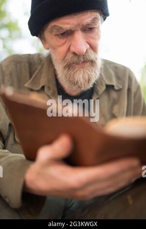 Close up portrait of old beardy man holding book in hands. Stock Photo