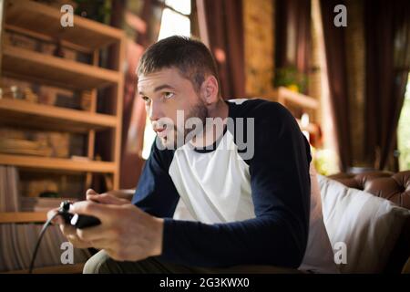 Side view of handsome young man holding game controller, playing video game. Stock Photo