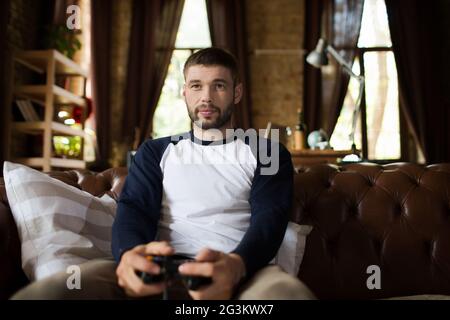 View of young man sitting on couch holding game controller joystick. Stock Photo