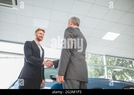 Beau homme en train de serrer la main avec le vendeur de véhicule. Banque D'Images