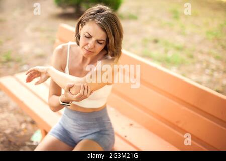 Femme sportive avec douleur au coude assise sur le banc dans le parc. Concept de fitness, de soins de santé et de médecine Banque D'Images