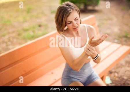 Femme sportive avec douleur de bras assis sur le banc dans le parc. Concept de fitness, de soins de santé et de médecine Banque D'Images