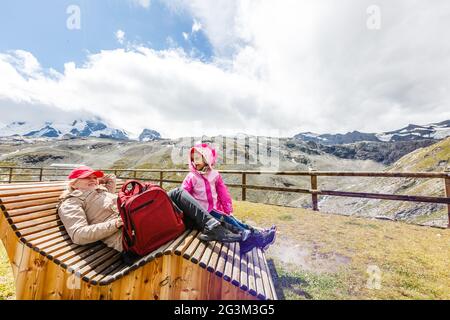 mère et fille avec sac à dos assis sur le sentier dans les montagnes à l'heure de la journée. Banque D'Images