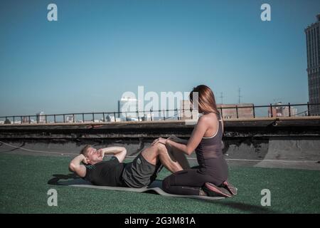 Jeune femme aidant l'homme avec des situps. Banque D'Images