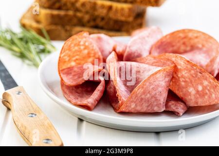 Tranché de salami fumé sur l'assiette sur la table blanche. Banque D'Images