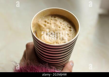La femme tient une tasse de voyage en bambou avec du café moussant et du lait de soja. Tasse à café Stripey sur le comptoir Banque D'Images