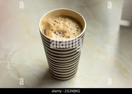 La femme tient une tasse de voyage en bambou avec du café moussant et du lait de soja. Tasse à café Stripey sur le comptoir Banque D'Images